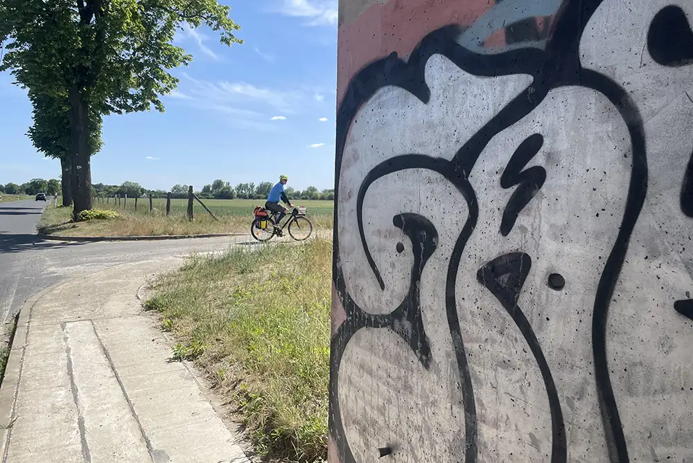 Mit Graffiti besprühte Ecke einer Unterführung, im Hintergrund der Rad-Begleiter
