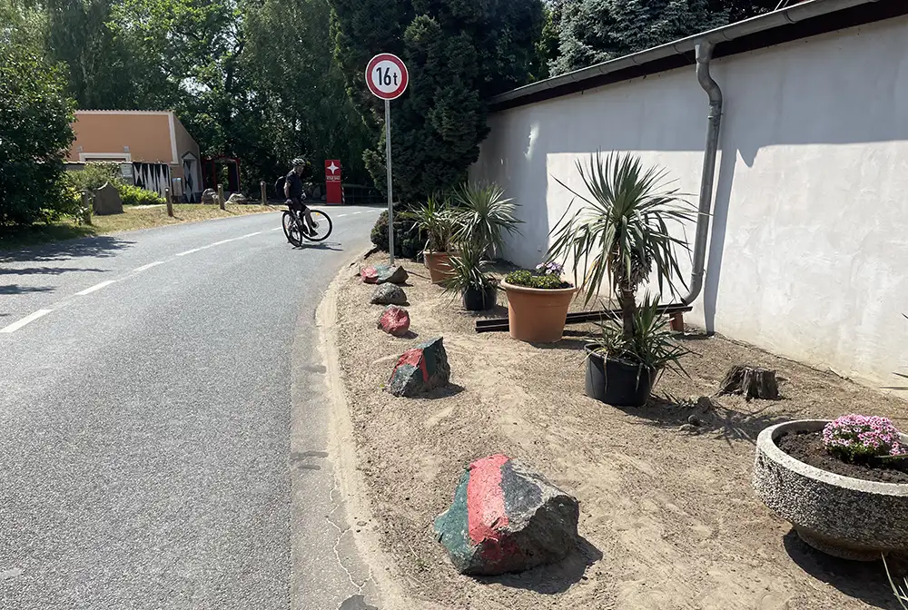Radfahrer wartet an einsamer Straße, am Rand bemalte Feldsteine und Palmen in Töpfen