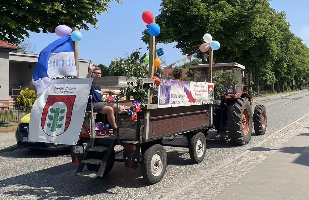 Vorbeifahrender Traktor mit Anhänger mit Luftballons und winkendem Mann