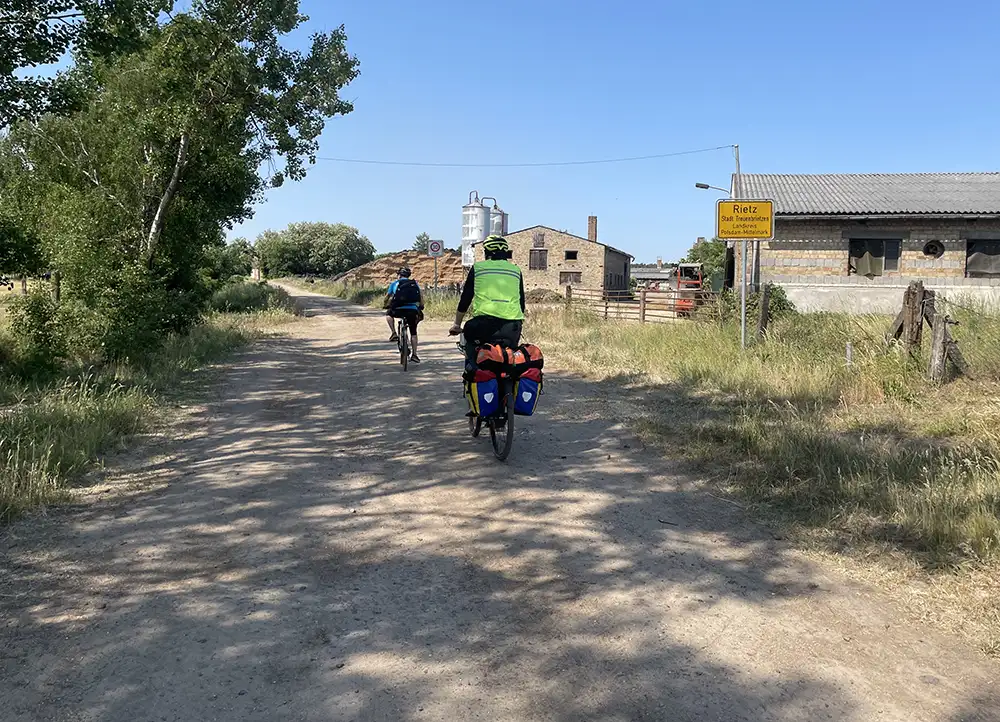 Zwei Radfahrer fahren auf breitem Feldweg am Ortsschild Rietz vorbei