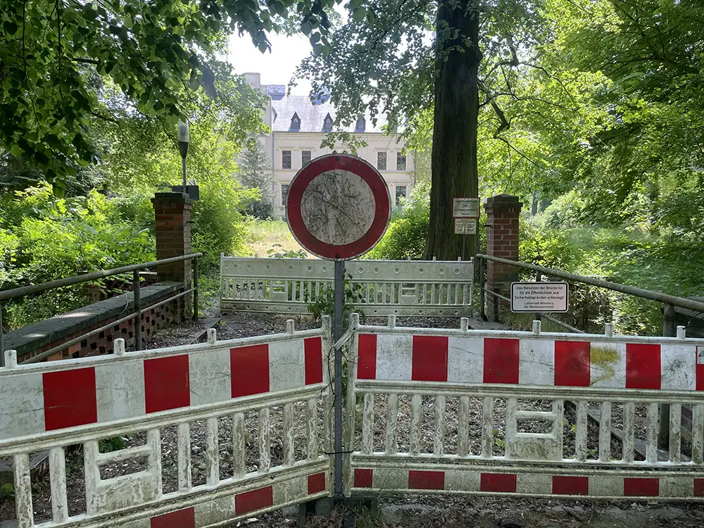 Rotweiße Kunststoff-Absperrgitter mit Einfahrt-Verboten-Schild vor einem alten Herrenhaus hinter Bäumen