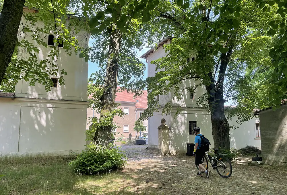 Toreinfahrt mit zwei turmartigen Gebäuden links und rechts, davor Radfahrer, der sein Fahrrad schiebt