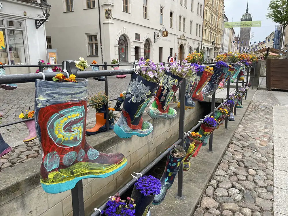 Metallgeländer an dem bunt bemalte Kinder-Gummistiefel, mit Blumen bepflanzt, hängen