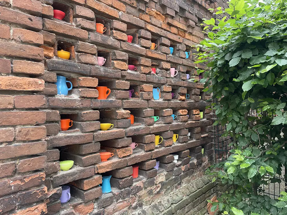 Einfarbige Tassen in rot, grün, gelb, blau, etc. arrangiert in Nischen einer Ziegelstein-Mauer