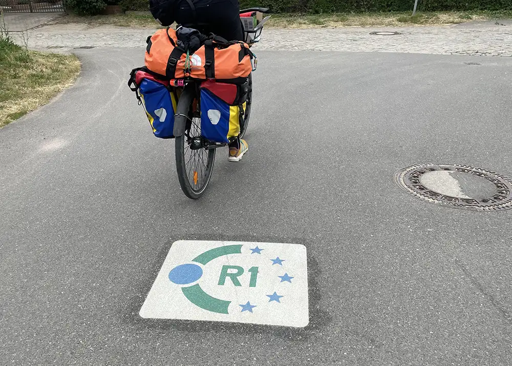 Auf dem Straßen-Asphalt markiertes Logo des Europa-Radwegs R1