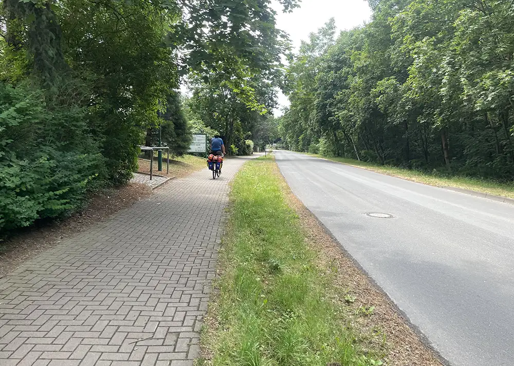 Gepflasterter Geh- und Radweg neben der Straße, mit Radfahrer weit voraus