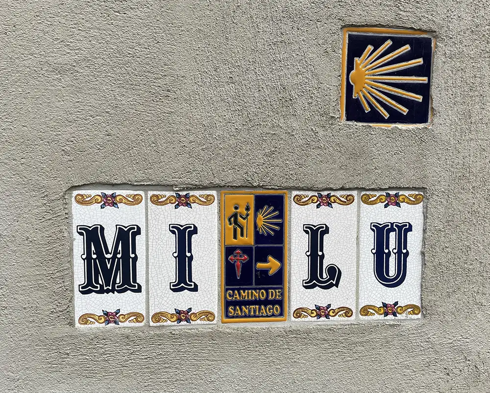 In eine verputzte Hauswand eingelassene, bemalte spanische Kacheln u.a. mit dem Namen „Santiago de Compostela“ und der Jakobsweg-Muschel