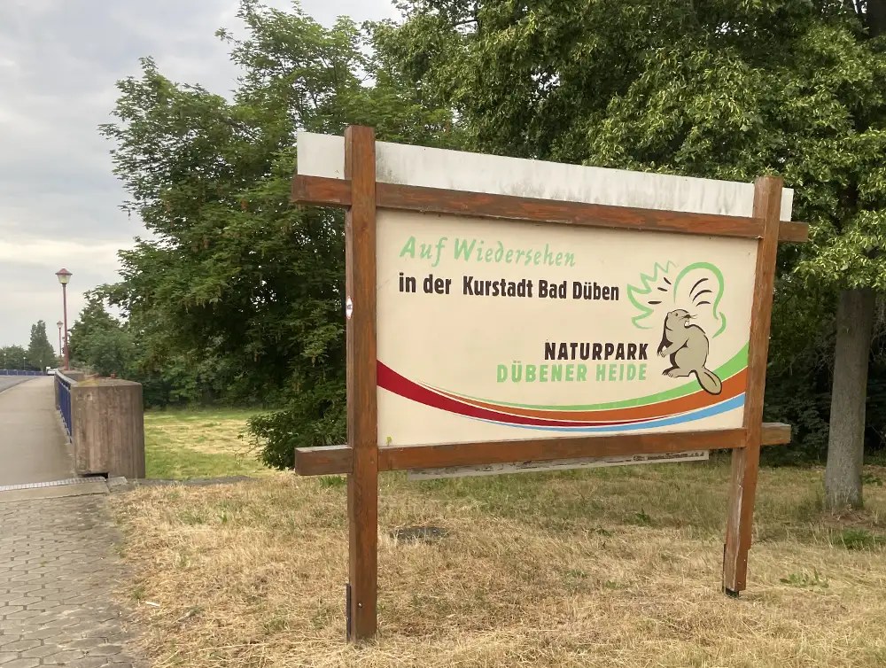 Mit Holzpfeilern eingerahmtes Schild „Auf Wiedersehen in der Kurstadt Bad Düben, Naturpark Dübener Heide“ mit einem Biber