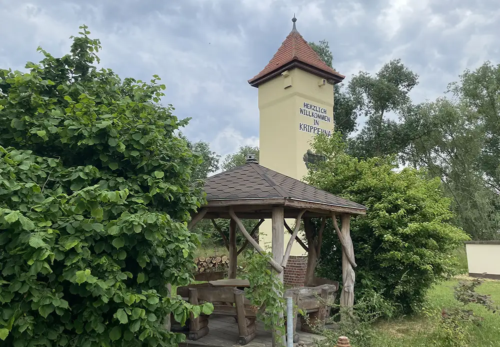 Rastplatz mit holzbänken, dahinter ein kleiner Turm mit Schrift Herzlich Willkommen in Krippehna