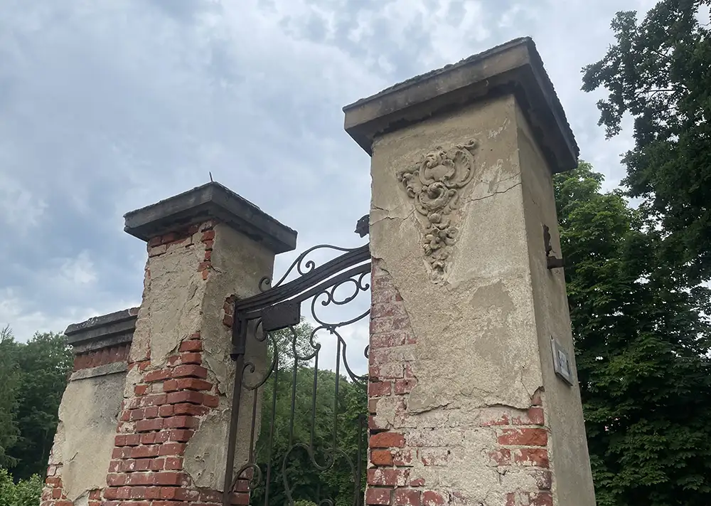 Schmiedeeisernes Tor zwischen zwei verfallenen gemauerten Pfeilern