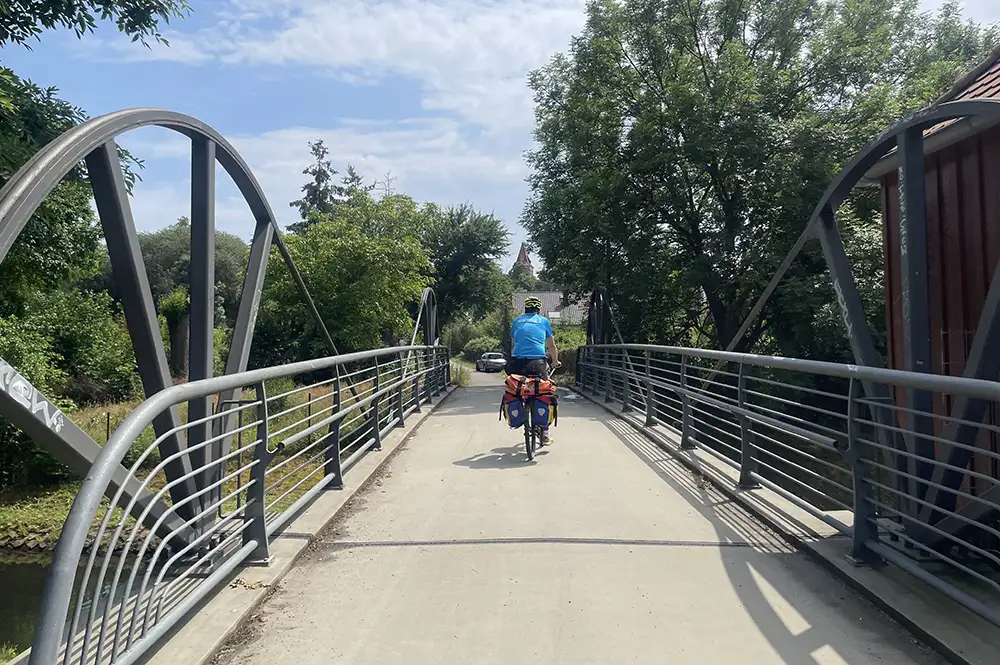 Fahrrad-Begleiter fährt über Fußgängerbrücke mit grau gestrichenem Metallgeländer und seitlichen Bögen