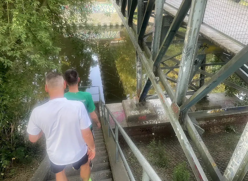 Zwei Läufer gehen eine Treppe neben einer Stahlkonstruktion-Brücke hinab