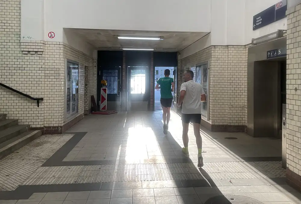 Läufer durchlaufen einen kleinen S-Bahnhof, durch den die Sonnenstrahlen hereinkommen