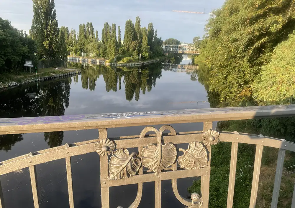 Blick von einer Brücke auf den Kanal, im Vordergrund das Metallgeländer mit einer Blumen-Verzierung