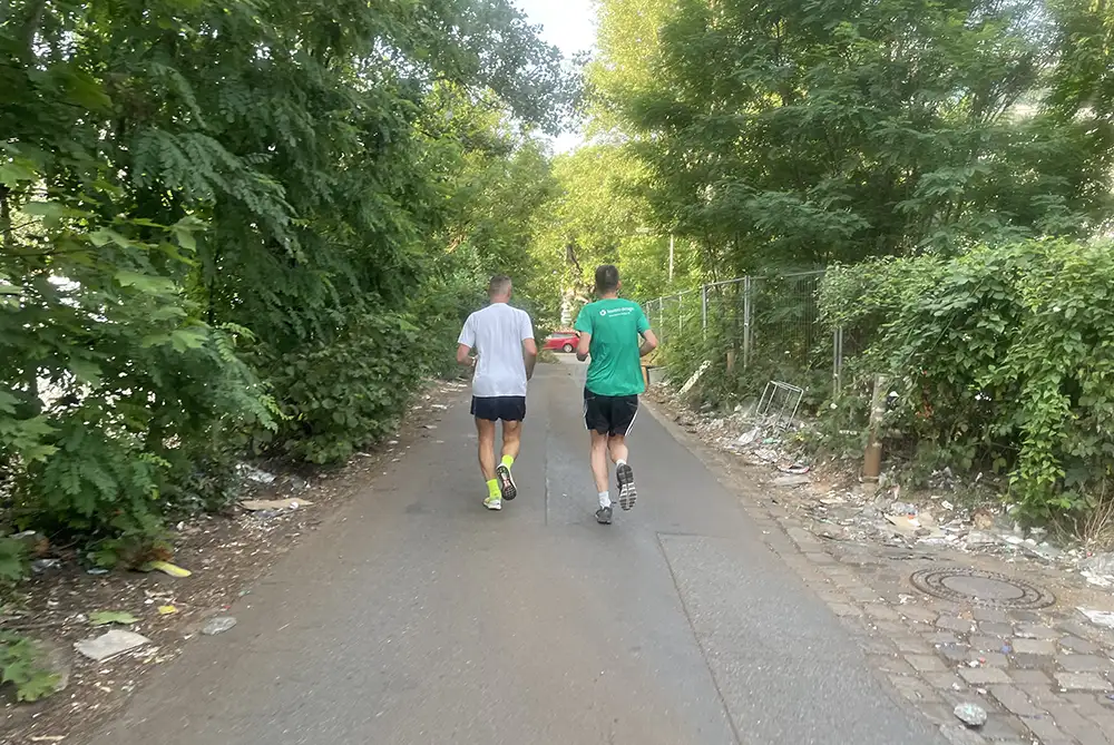 Zwei Läufer auf einem schmalen Asphaltweg, an dessen Seiten Müllreste liegen