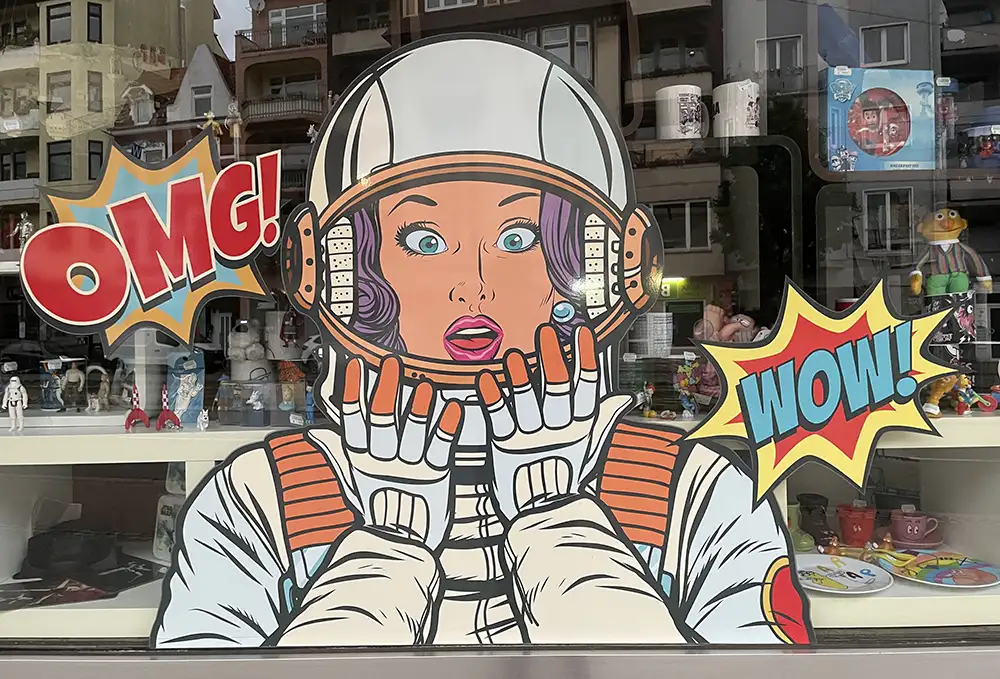 Große Comic-Figur auf der Fensterscheibe eines Geschäfts: Astronautin wundert sich mit OMG und WOW