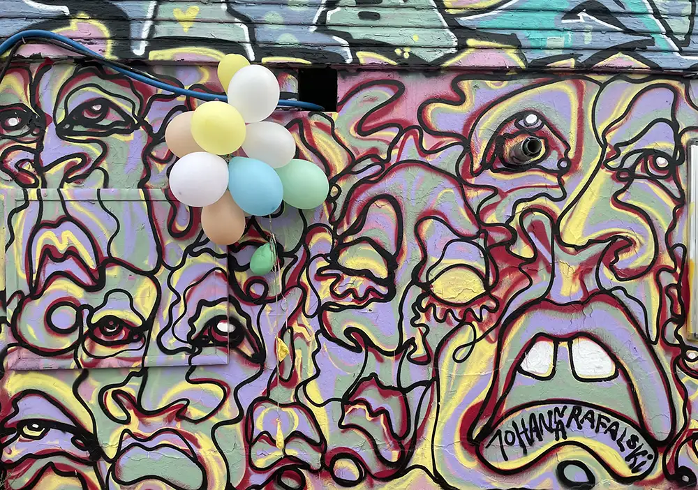 Luftballons an einer mit Graffiti-Gesichtern vollständig bemalten Mauer