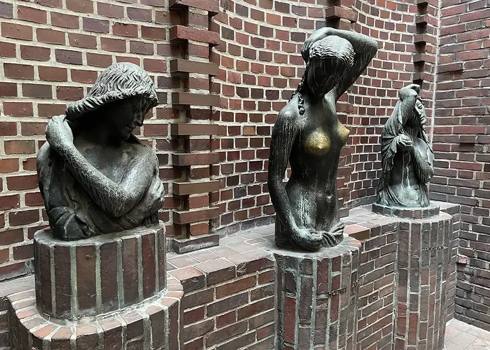Drei Bronze-Büsten vor einer Backstein-Mauer