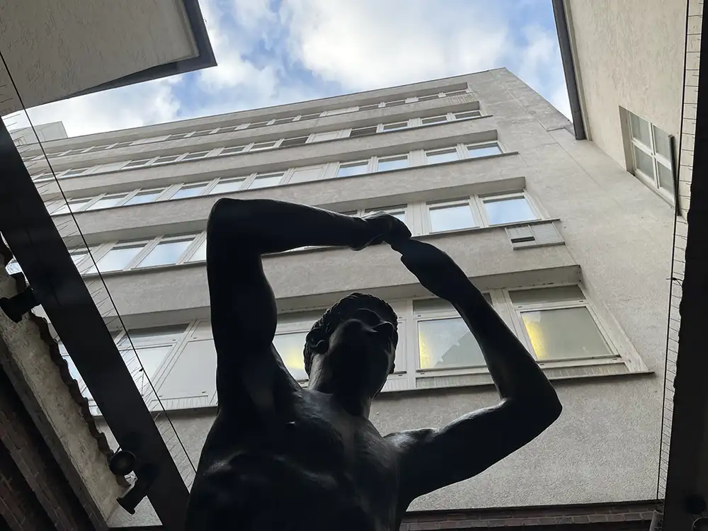 Dunkler Umriss einer Skulptur vor einem modernen Gebäude, darüber der Himmel
