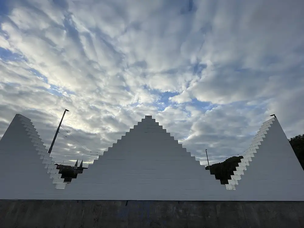 Skulptur Three Triangles vor einem dramatischen Wolkenhimmel