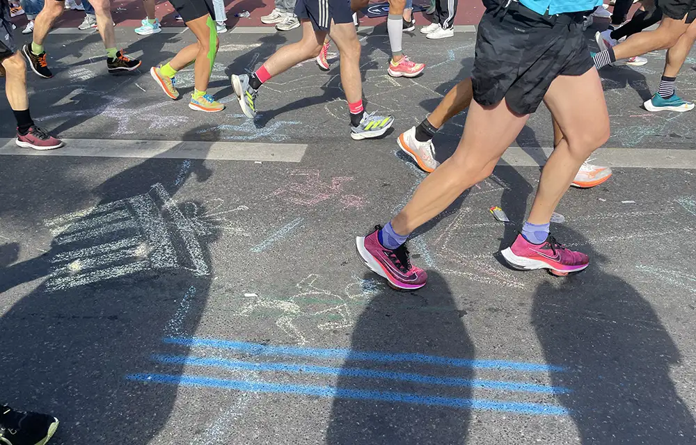 Blick auf den mit Kreidezeichnungen geschmückten Asphalt und die Schuhe und Beine der Läufer*innen