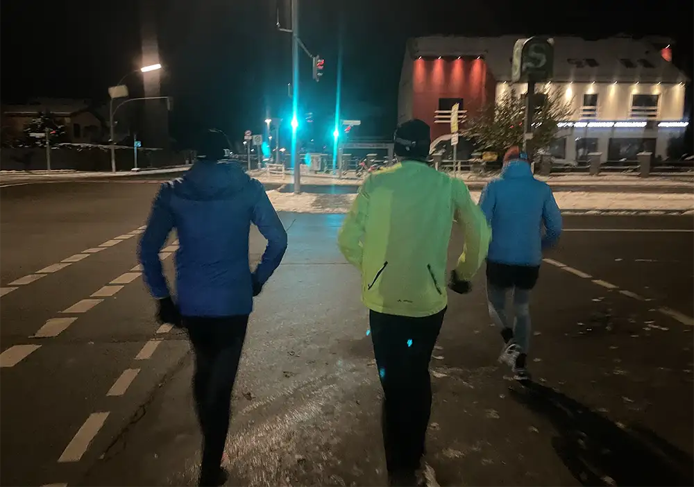 Drei Läufer überqueren im Morgendunkel bei Grün eine breite Straße