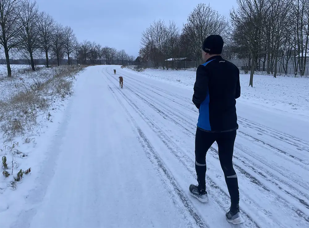 Läufer mit Hunden auf einer verschneiten einsamen Straße