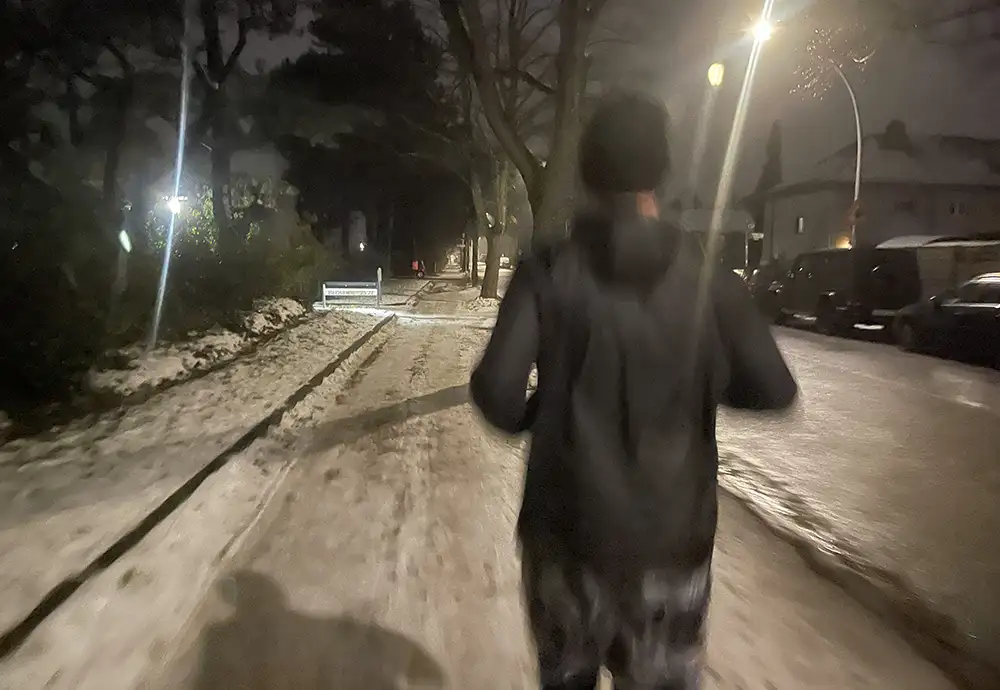 Läufer auf Schnee- und eisbedecktem Fußweg an einer Wohnstraße