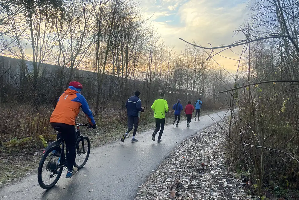 Läufergruppe mit Fahrradbegleitung auf einem asphaltierten schmalen Weg