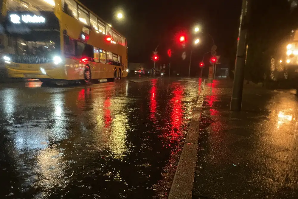 Regennasse Straße im Dunkeln, die roten Ampellichter spiegeln sich im nassen Asphalt