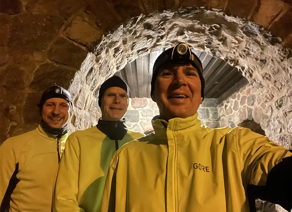 Drei Läufer in neongelben Jacken posieren vor einem Feldstein-Kircheneingang