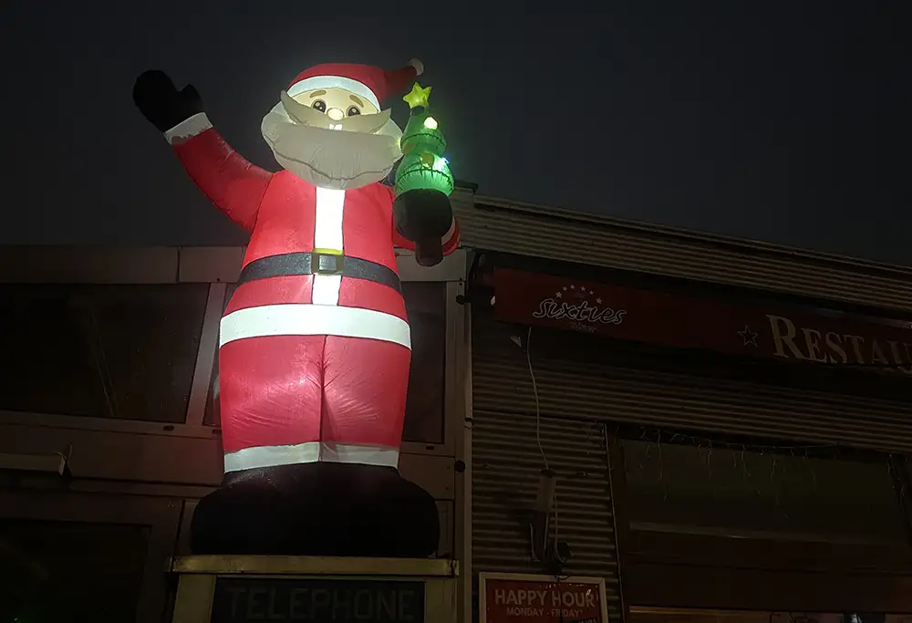 Großer aufgeblasener Weihnachtsmann, der mit einer Hand winkt, an der Fassade eines Restaurants