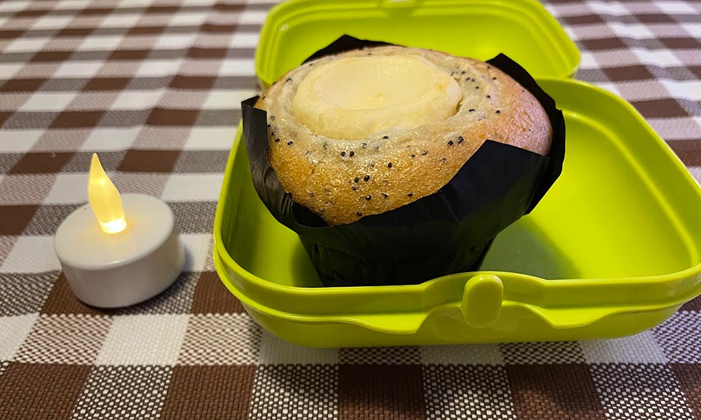 Großer Muffin in einer offenen Dose, daneben ein elektrisches Teelicht