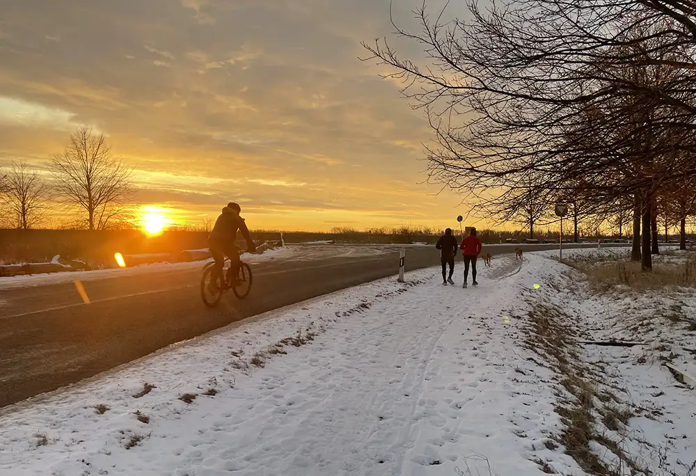 Läufer und Radfahrer im Gegenlicht der gleißend gelb aufgehenden Sonne