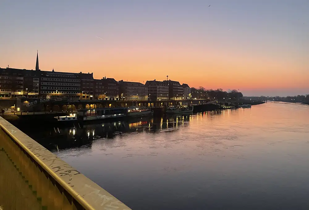 Rötlicher Sonnenaufgang über den Häusern am Ufer der Weser