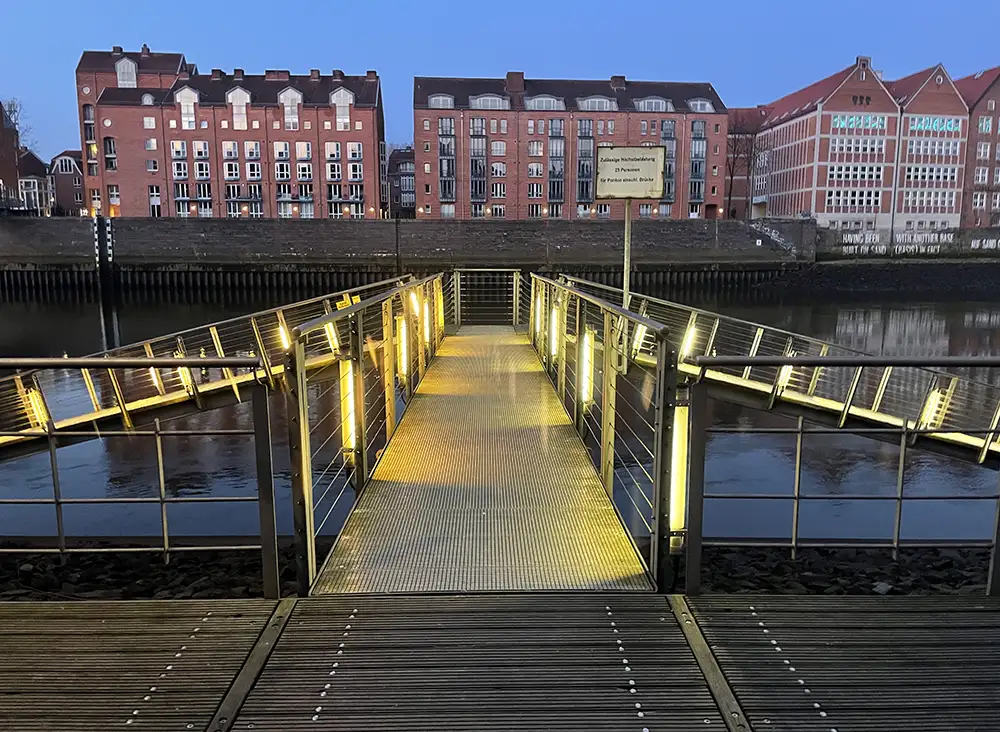 Steg mit gelb leuchtenden Neonröhren an der Weser am frühen Morgen