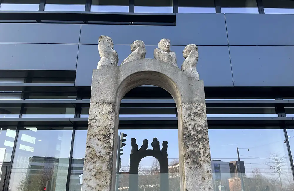 Kunstobjekt mit vier Männer-Torsos auf einem Torbogen vor einem Bürogebäude