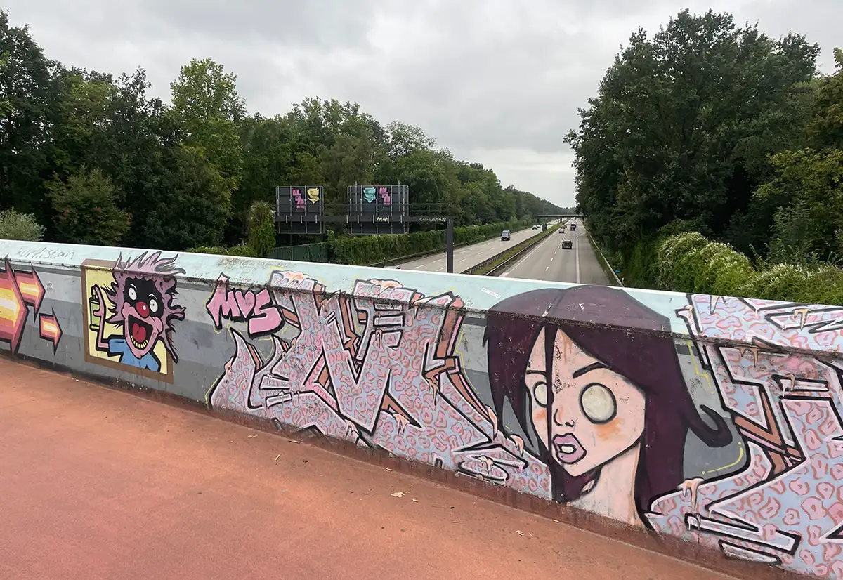 Graffiti an der Metallbrüstung, dahinter Blick auf die Autobahn
