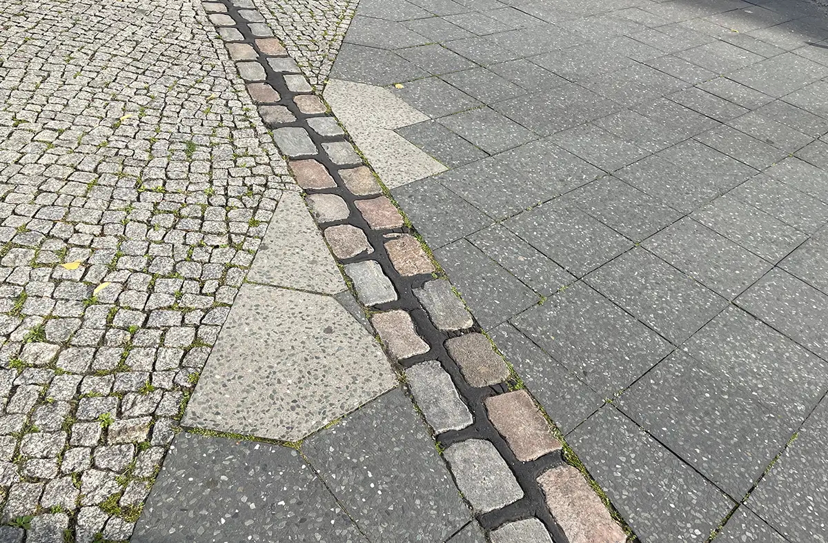 Quer verlaufende 2-zeilige Kopfstein-Reihe auf dem Fußweg, die den ehemaligen Verlauf der Berliner Mauer markiert