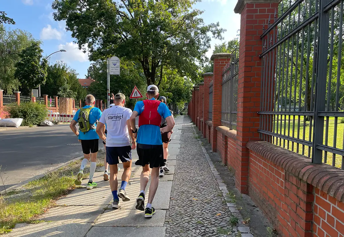 Laufgruppe auf einem Fußweg entlang eines hohen schmiedeeisernen Zauns mit Backstein-Pfeilern