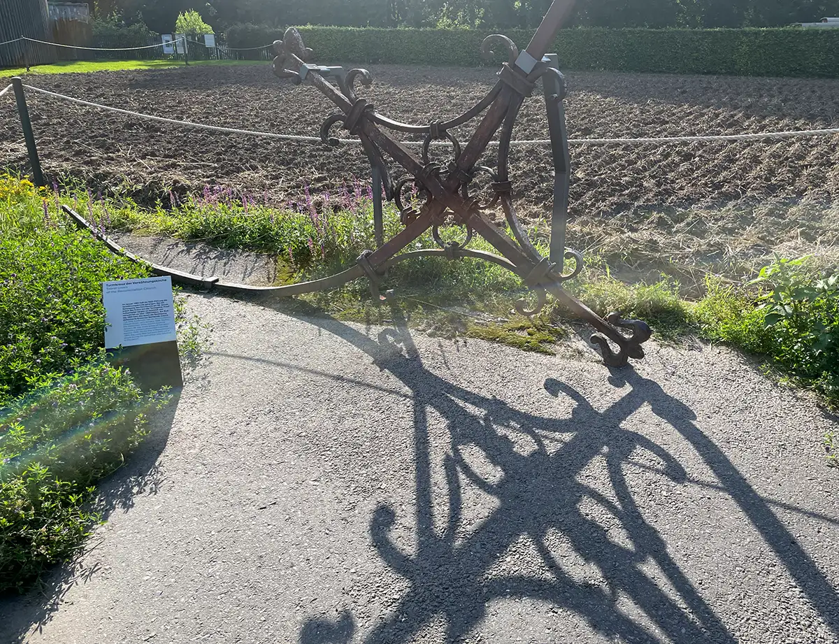 Ehemaliges Turmkreuz aus geschwungenem rostigen Metall liegt am Wegesrand und wirft Schatten