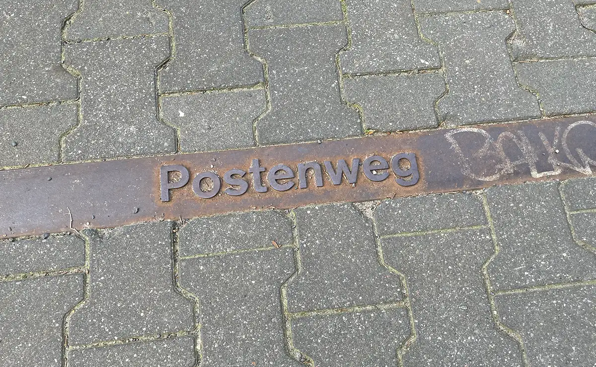 In den Fußweg eingelassene Metallplatte mit Beschriftung Postenweg