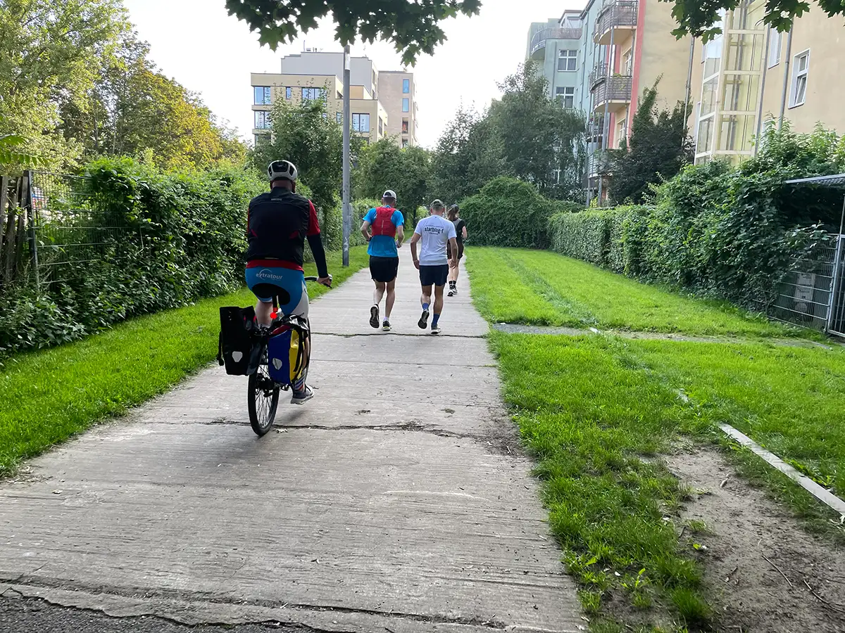 Laufgruppe mit Radbegleiter auf einem historischen Plattenweg zwischen moderner Wohn-Bebauung