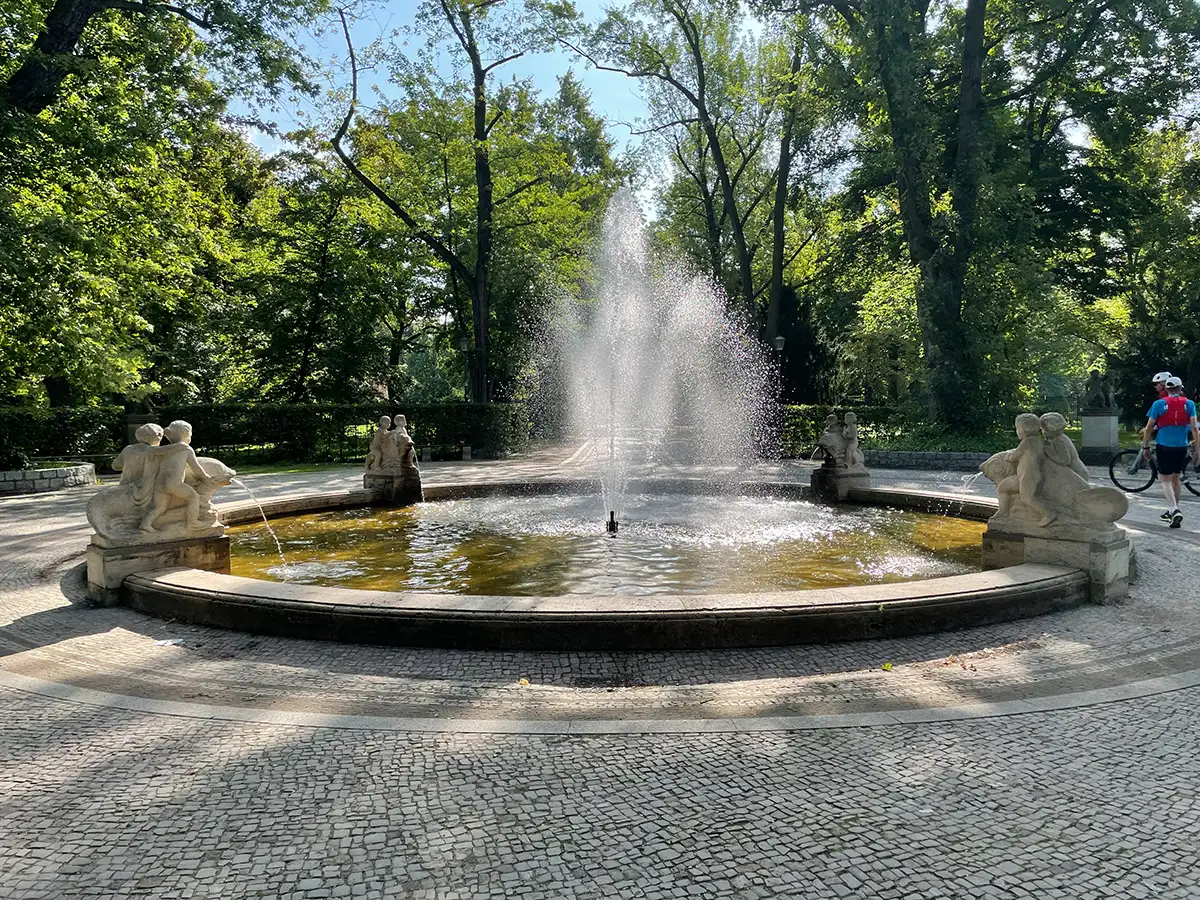 Großes Becken mit Springbrunnen und 4 Steinskulpturen im Gegenlicht