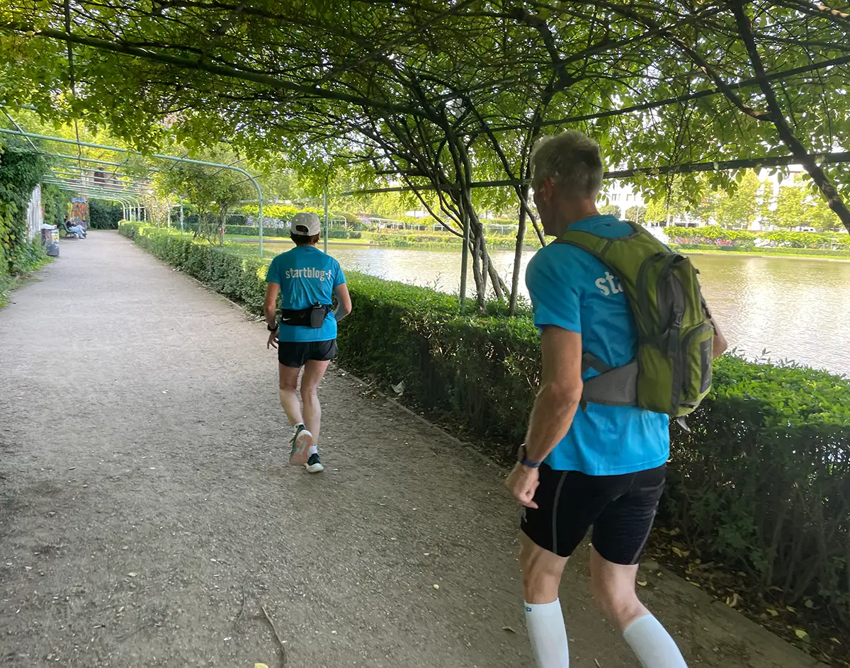 Läuferin und Läufer in hellblauen startblog-f-Shirts unter einem Laubengang am Engelbecken