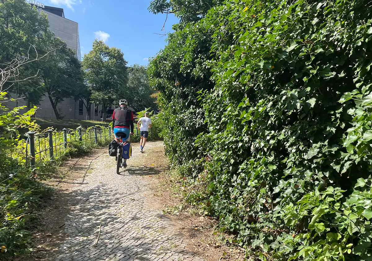Läufer und Radbegleiter biegen um die Ecke einer efeubewachsenen Mauer