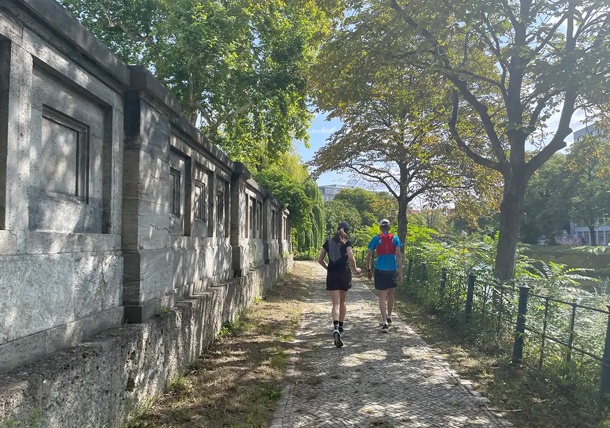 Läuferin und Läufer auf einem Weg neben einer alten Mauer
