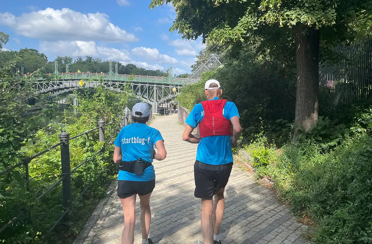 Läuferpaar in blauen startblog-f-Shirts läuft am Ufer auf die Lichtensteinbrücke zu