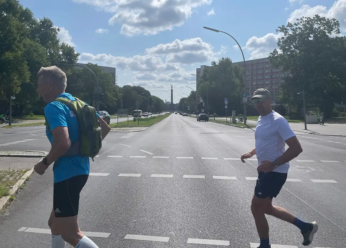 Läufer überqueren eine breite Straße, im Hintergrund ist die Siegessäule zu sehen