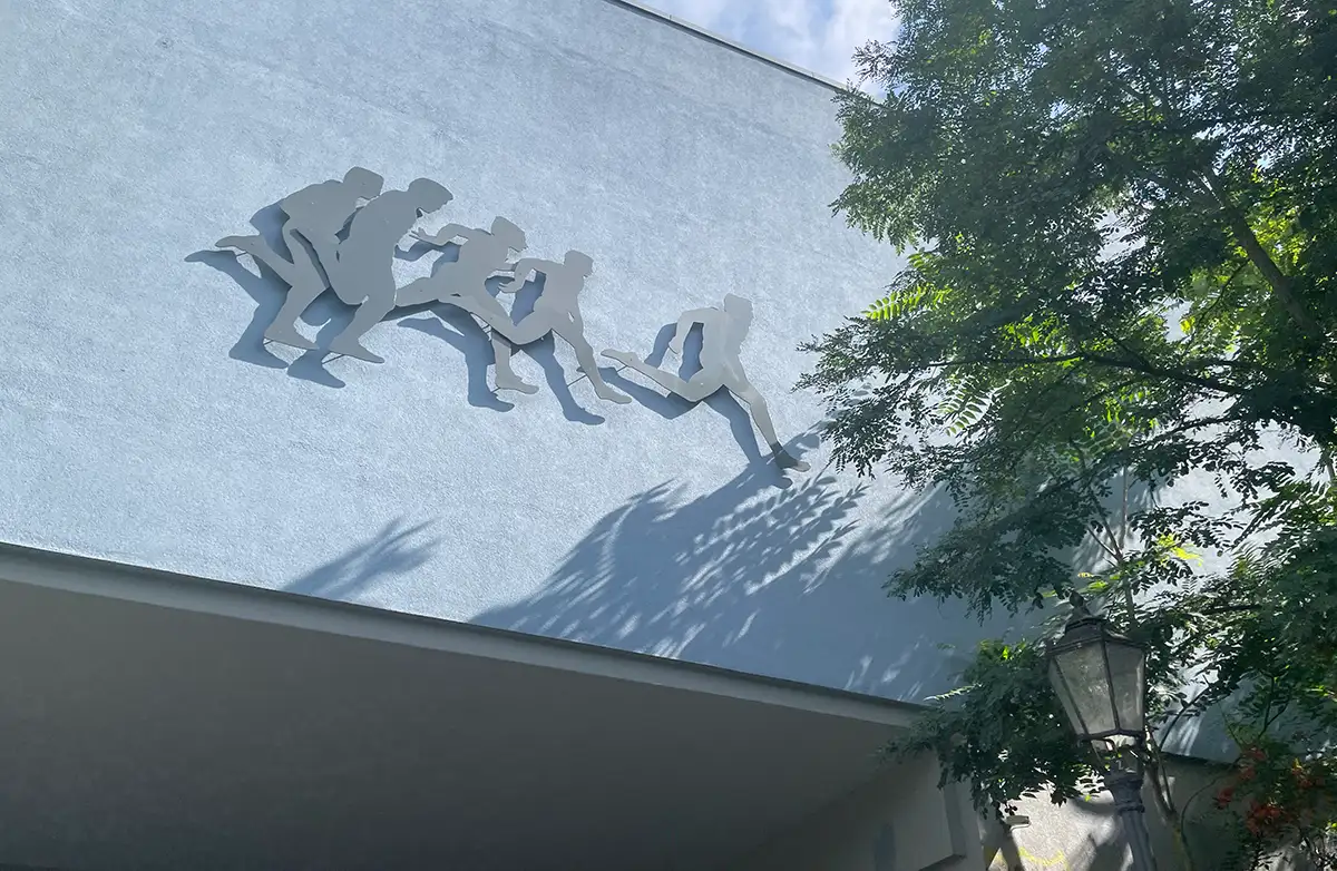 Metall-Silhouetten oben an einem Gebäude zeigen 5 sprintende Läufer